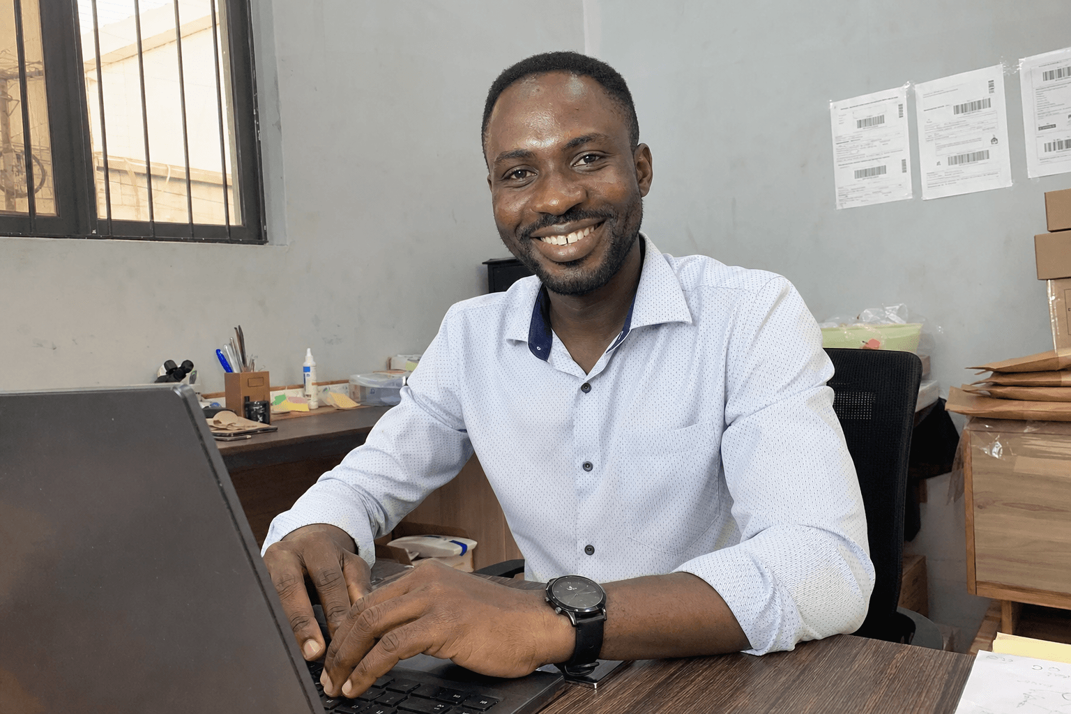 Bola smiling at his desk in a tidy Abuja office